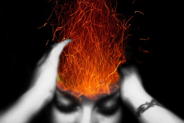 A woman holds her head as fire erupts from it in frustration. 