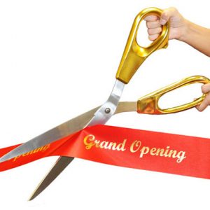 giant gold scissors cutting a red ribbon with "grand opening" on it